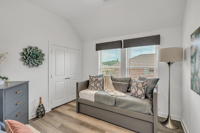 sitting room with baseboards, visible vents, light wood finished floors, and lofted ceiling