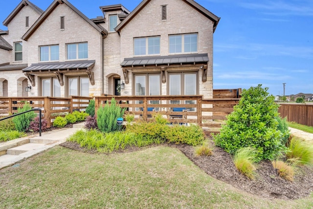view of front facade featuring a standing seam roof, metal roof, a front yard, fence private yard, and brick siding
