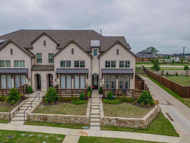 view of front of home featuring a standing seam roof, a shingled roof, a front lawn, and brick siding