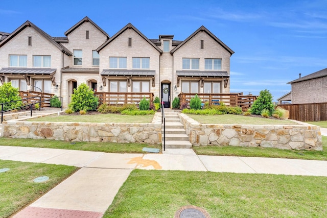 view of property featuring brick siding, a front lawn, and fence