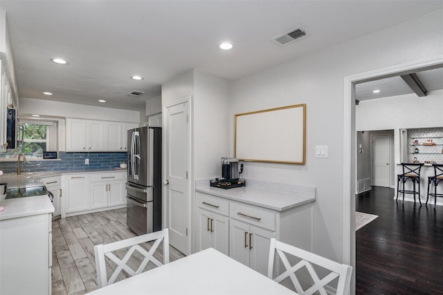 kitchen featuring stainless steel refrigerator with ice dispenser, visible vents, tasteful backsplash, white cabinets, and light wood-style floors