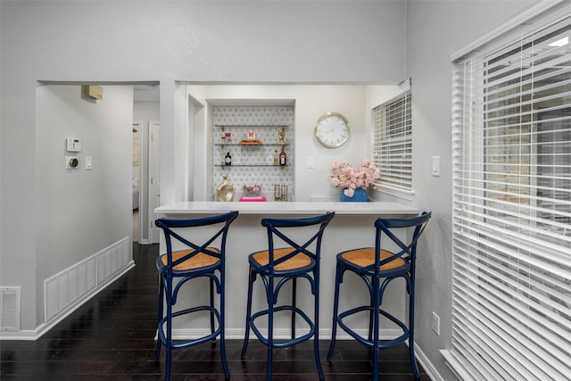 interior space featuring visible vents, wet bar, baseboards, and dark wood-style floors