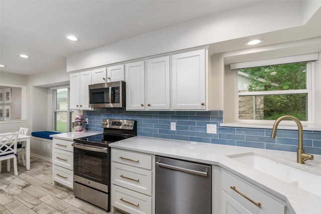 kitchen with decorative backsplash, light countertops, white cabinetry, a sink, and stainless steel appliances