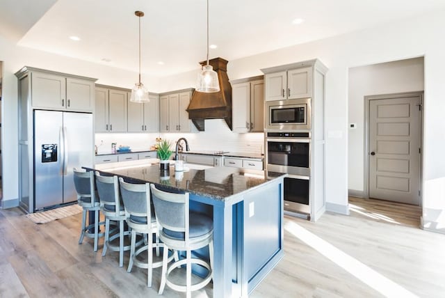 170 Rolling Hills Blvd, Alvord, TX 76225 - kitchen featuring decorative backsplash, appliances with stainless steel finishes, light wood-type flooring, dark stone counters, and an island with sink