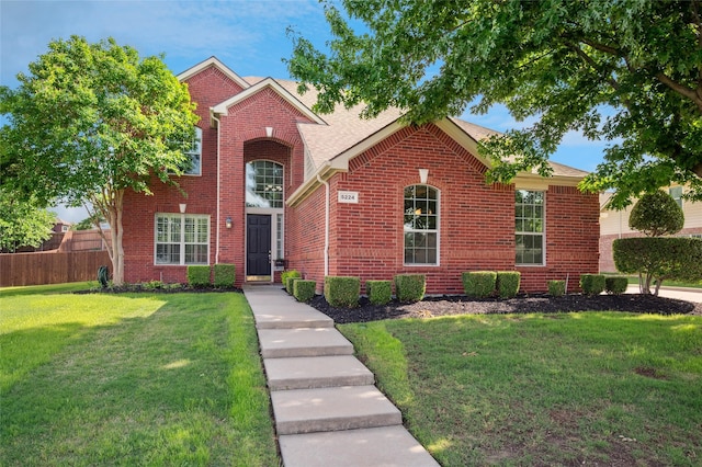 traditional-style house featuring brick siding, fence, a front yard, and roof with shingles