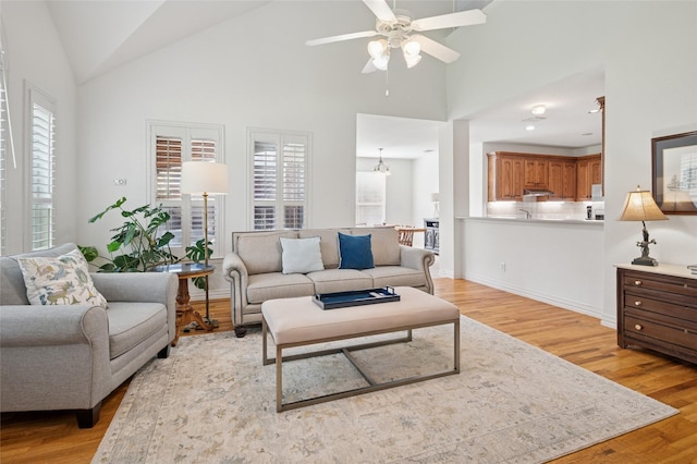 living area with high vaulted ceiling, ceiling fan, and light wood finished floors