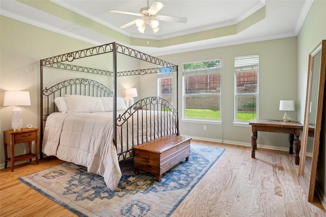 bedroom with baseboards, a tray ceiling, ornamental molding, and wood finished floors