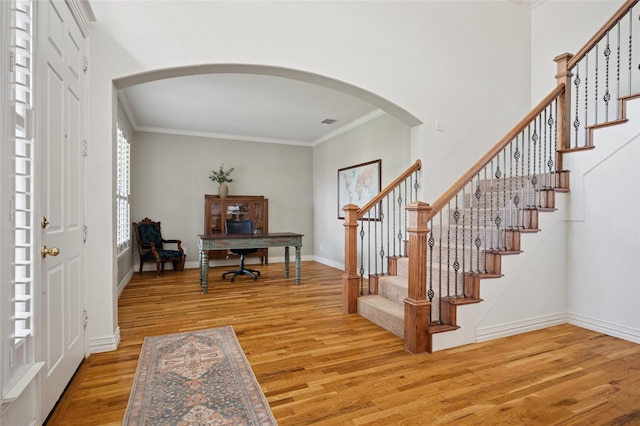 entryway with light wood-type flooring, arched walkways, crown molding, and stairway