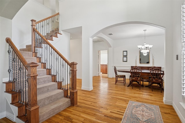 stairway featuring arched walkways, a chandelier, baseboards, wood finished floors, and visible vents