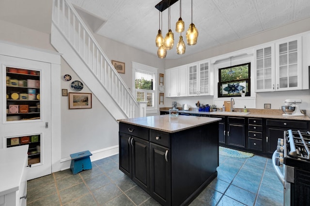 kitchen featuring stainless steel gas range, white cabinets, dark cabinets, a sink, and a notable chandelier