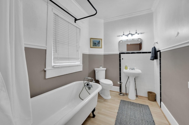 full bath with a freestanding tub, tile walls, wood finished floors, toilet, and ornamental molding