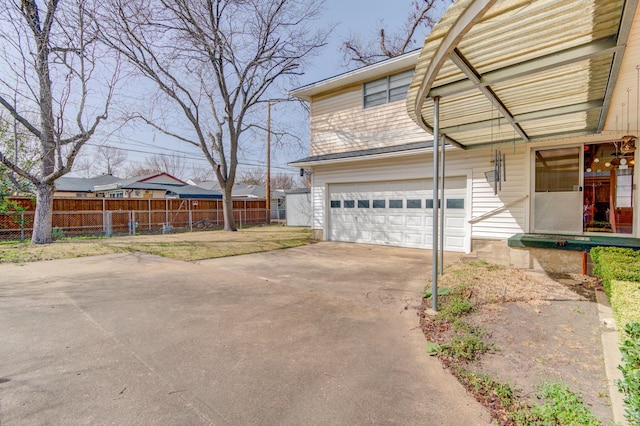 view of side of home featuring an attached garage, concrete driveway, and fence