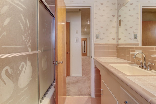 bathroom with vanity, combined bath / shower with glass door, and wallpapered walls