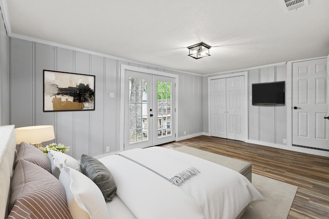 bedroom with crown molding, a decorative wall, french doors, wood finished floors, and visible vents
