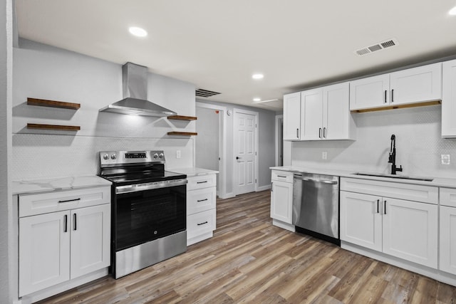 kitchen featuring visible vents, appliances with stainless steel finishes, open shelves, a sink, and wall chimney exhaust hood