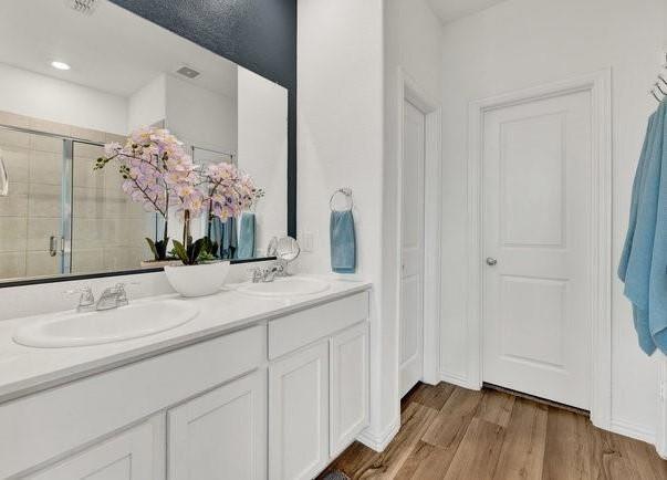 full bath featuring double vanity, a shower stall, a sink, and wood finished floors