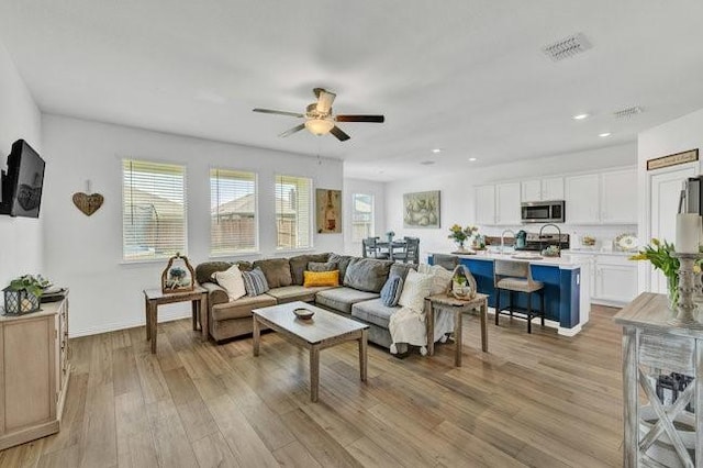 living area with plenty of natural light, a ceiling fan, light wood finished floors, and visible vents