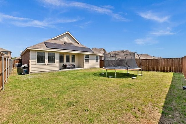 back of house featuring a fenced backyard, a trampoline, a yard, and solar panels