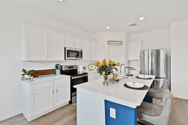kitchen with a breakfast bar, light wood-style floors, stainless steel appliances, white cabinetry, and decorative backsplash