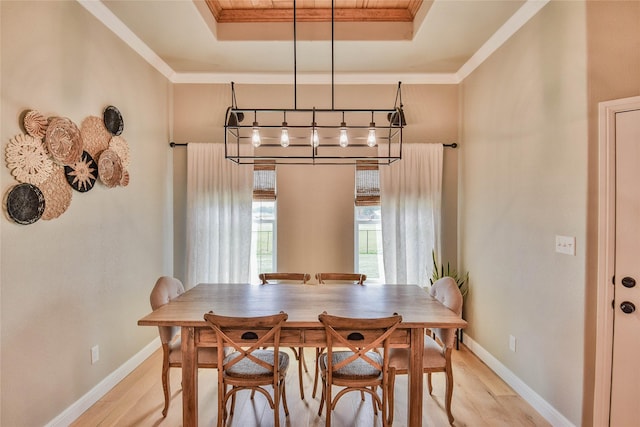 dining space featuring a tray ceiling, ornamental molding, baseboards, and light wood finished floors