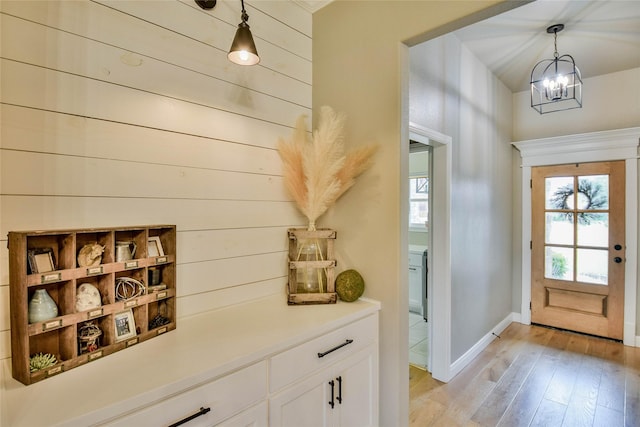 doorway featuring baseboards, light wood-type flooring, and a chandelier