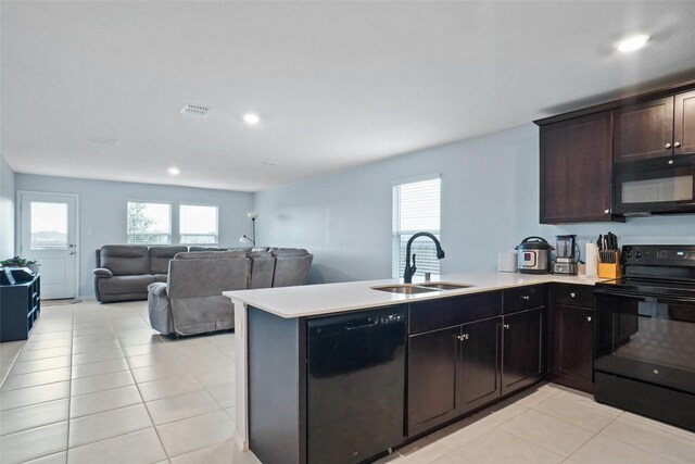 kitchen featuring a peninsula, a healthy amount of sunlight, a sink, light tile patterned floors, and black appliances