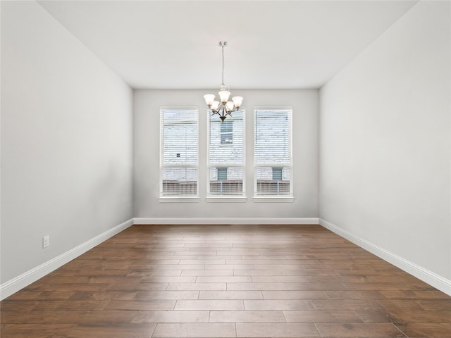 spare room featuring baseboards, a chandelier, and dark wood-style floors