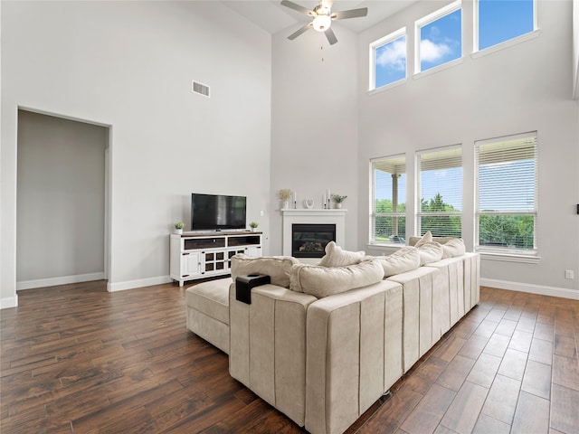 living room with visible vents, dark wood-style flooring, ceiling fan, and a high ceiling