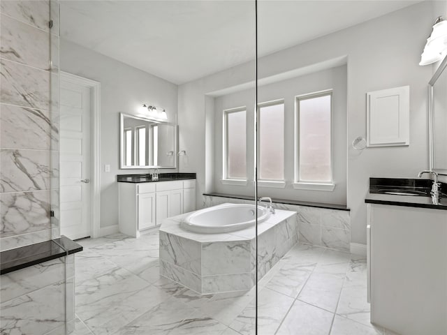 full bathroom featuring a sink, marble finish floor, baseboards, two vanities, and a garden tub