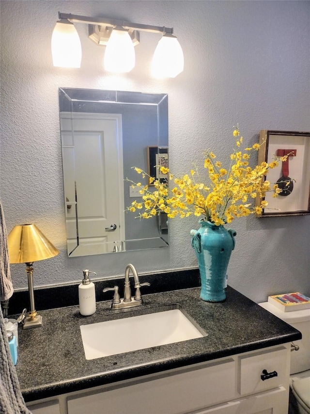 bathroom with toilet, a textured wall, and vanity