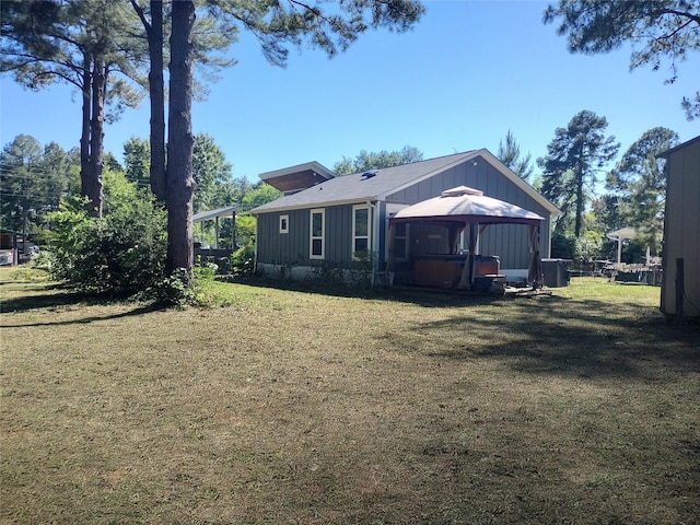 rear view of house with a hot tub, a yard, board and batten siding, and a gazebo