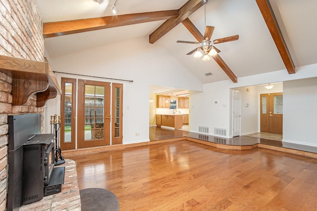 unfurnished living room with visible vents, a wood stove, wood finished floors, and beam ceiling