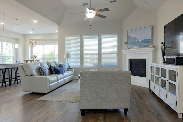 living room featuring a ceiling fan, vaulted ceiling, a glass covered fireplace, and dark wood-type flooring