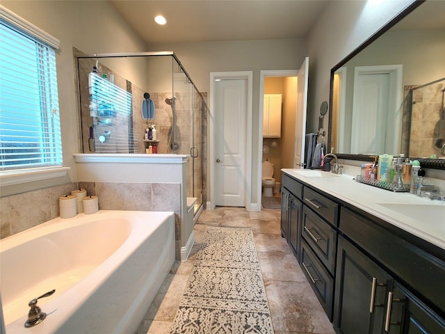 bathroom featuring a sink, double vanity, toilet, a shower stall, and a garden tub