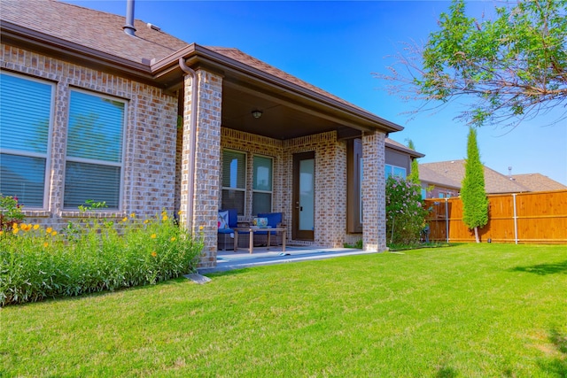 back of house featuring a lawn, brick siding, fence, and a patio area