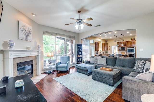 living room with a fireplace, dark wood-style flooring, a ceiling fan, and visible vents