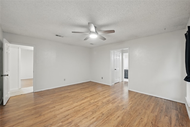 spare room featuring a textured ceiling, light wood-style flooring, a ceiling fan, baseboards, and visible vents