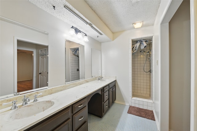 full bath with double vanity, a textured ceiling, tiled shower, and a sink