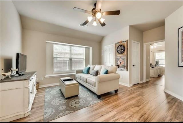 living room with baseboards, a ceiling fan, and light wood-style flooring