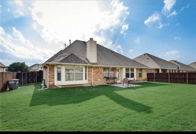 back of house with a fenced backyard, a chimney, a yard, and brick siding