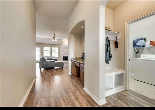 corridor featuring baseboards, arched walkways, light wood-style flooring, and washer / clothes dryer