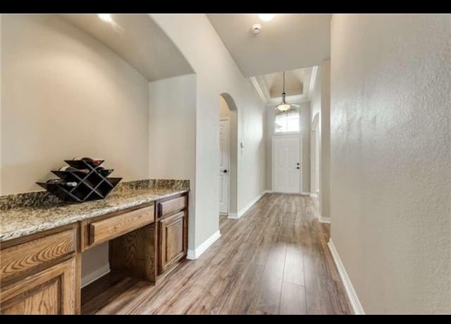 corridor with baseboards, arched walkways, and light wood finished floors
