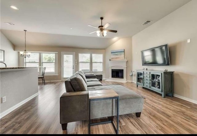 living room with ceiling fan with notable chandelier, baseboards, wood finished floors, lofted ceiling, and visible vents