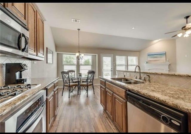 kitchen with appliances with stainless steel finishes, a sink, lofted ceiling, light wood-type flooring, and backsplash