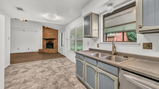 kitchen with a sink, dishwasher, a brick fireplace, a textured ceiling, and visible vents