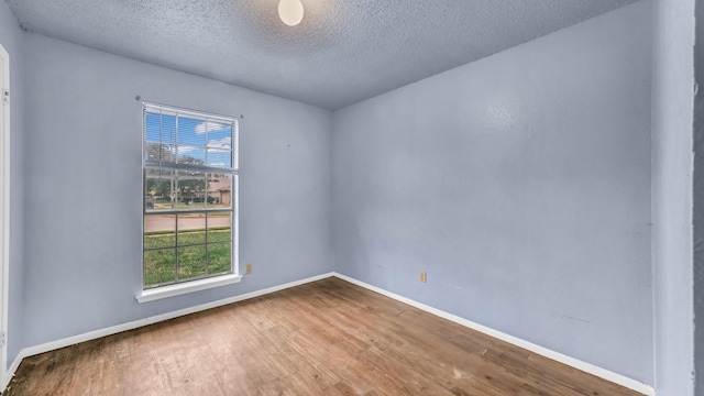 spare room featuring baseboards, a textured ceiling, a healthy amount of sunlight, and wood finished floors