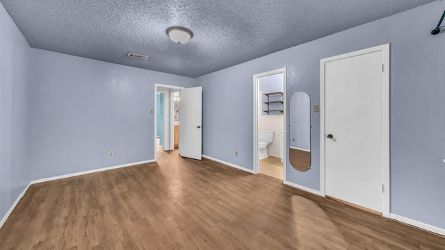 unfurnished bedroom featuring a textured ceiling, visible vents, wood finished floors, baseboards, and ensuite bathroom