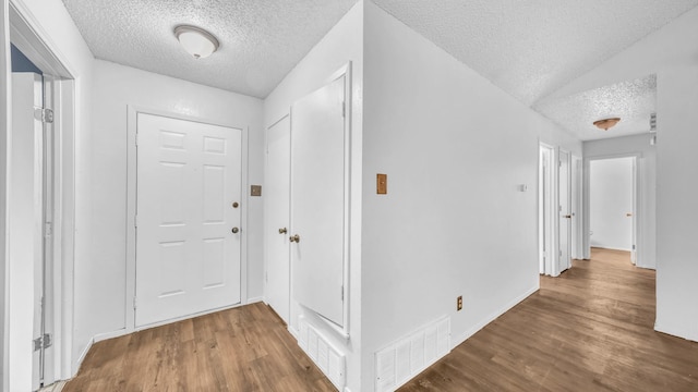 hall with visible vents, a textured ceiling, and wood finished floors