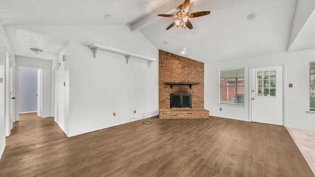 unfurnished living room featuring a ceiling fan, a brick fireplace, wood finished floors, a textured ceiling, and lofted ceiling with beams