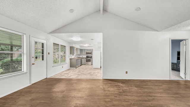 unfurnished living room featuring a sink, a textured ceiling, high vaulted ceiling, baseboards, and wood finished floors